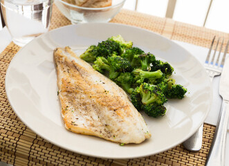 Fried fillet of sea bass with garnish of broccoli on black warm stone plate