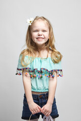 A happy little girl with long light hair and a white basket of flowers, in a turquoise blouse and blue denim shorts on white background. Smiling child