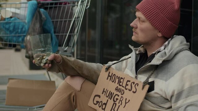 Medium shot of desperate poor man begging for money sitting with sign homeless and hungry at street