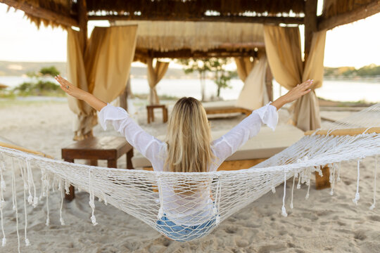 The girl is resting in a hammock on the beach near the blue ocean