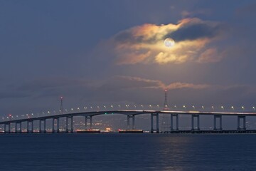 Fototapeta na wymiar a long bridge going over the ocean with a moon shining Moonrise over Bridge, San Francisco Bay Area
