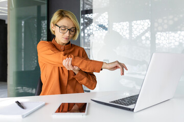 Office worker woman has severe pain in hand joints, long sitting work in business woman at workplace with laptop inside office.