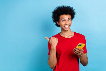 Portrait of cheerful positive person wear red t-shirt hold smartphone indicating at sale empty space isolated on blue color background