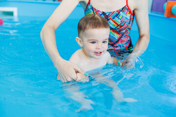 Fototapeta na wymiar A 2-year-old little boy learns to swim in a clean pool. Child development. Developmental pool for teaching children to swim. Swimming school
