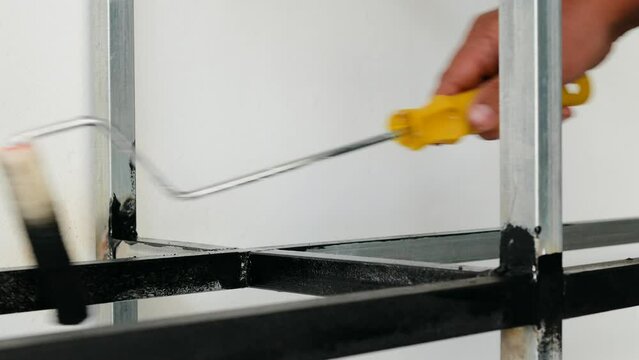 A man using a roller to paint black on galvanized steel