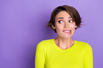 Portrait of nice worried young lady biting lips look nervous puzzled empty space isolated on purple...