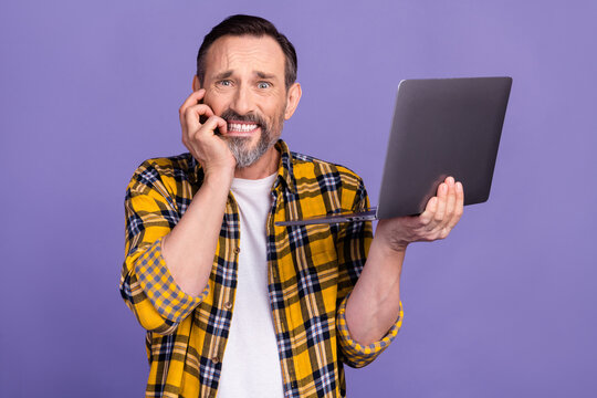 Photo of stressed nervous man wear checkered clothes bite hand use modern macbook sorry oops mistake isolated on purple color background