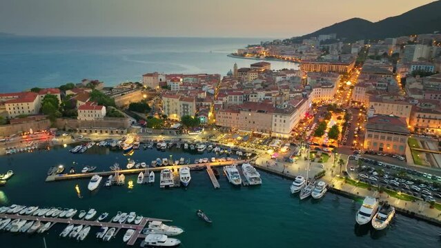Flying over harbor, old houses and city lights in Ajaccio - capital of Corsica, France. Aerial evening shot of Ajaccio old town, Corsica island