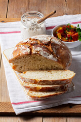 Round yeast bread made from white and whole grain flour, tomato salad and pate on a wooden background. Rustic style.