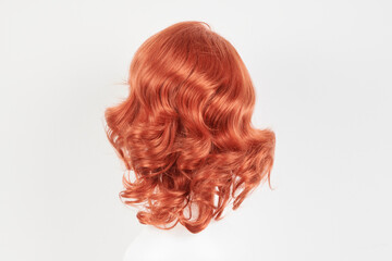 Natural looking ginger wig on white mannequin head. Medium length hair with wavy curls on the plastic wig holder isolated on white background, back view.