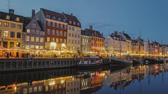 Panning evening shot of Nyhavn canal New Harbour with colorful houses and sailing boats in Copenhagen. 4K HDR shot. People walk along the canal, Copenhagen, Denmark