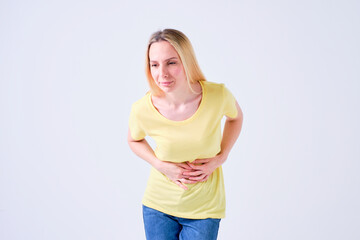 young blonde girl with stomach ache or intestinal discomfort in yellow t-shirt on white background