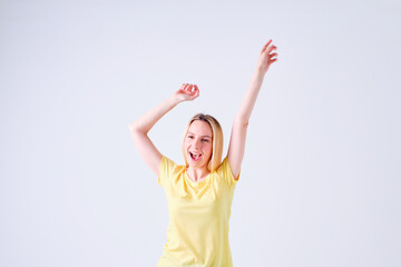 cheerful young blonde girl celebrating with arms up in yellow t-shirt on white background