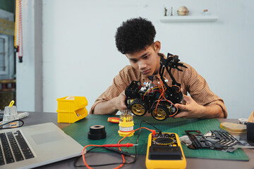 Asian young man assembling a robotic car, focus on robotics, assembling a robotic robot to develop intelligent robotics, mechanics students assembling a rescue robot car. Surveillance Robot.