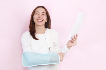 
Patient with broken arm in sling, Asian woman in casual white shirt broken hand wearing an arm brace standing over pink background with copy space.