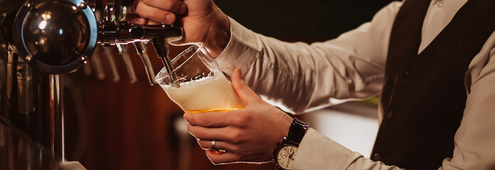 hands of bartender pour into glass draught light foamy beer from tap in bar