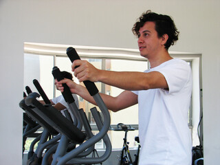 Curly and healthy man doing exercise on an elliptical gym machine