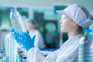 scientist worker checking the quality of water bottles on the machine conveyor line at the industrial factory. Female worker recording data at the beverages manufacturing line production.