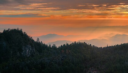 a sky filled with a very orange sunset behind mountains and trees