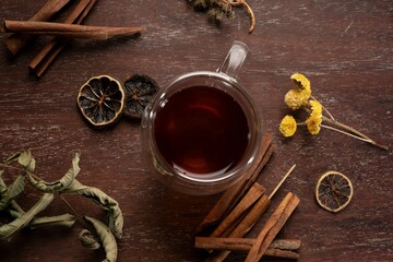Top-down shot of a steaming cup of tea placed beside two cinnamon sticks and two dried lemon slices