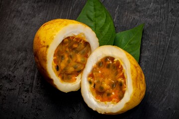 Ripe passion fruit cut in half, resting on a wooden table top with green foliage in the background