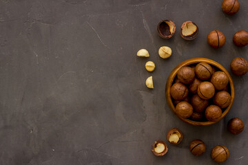 Wooden bowl of raw macadamia nuts in shell. Healthy protein snack background - obrazy, fototapety, plakaty