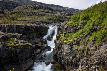 Beautiful Fossardalur waterfall cascading down a rocky cliff in the middle of a picturesque valley