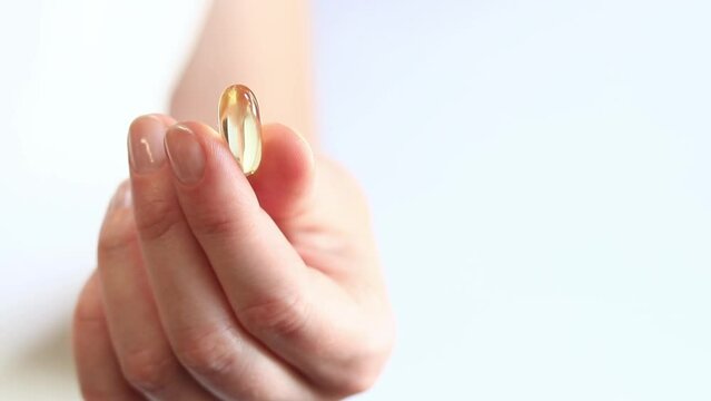 Medicine capsule in female hands, Omega-3. Bright yellow transparent vitamins on a white background. Medicine and healthcare. Vitamins and dietary supplements. Omega 3 Gold Fish Oil Capsule