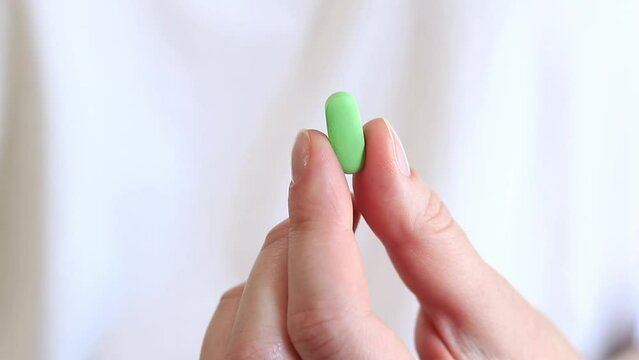Vitamins on a white background. The hand holds one green pill with two fingers. The concept of medicine and health. Vitamins and dietary supplements