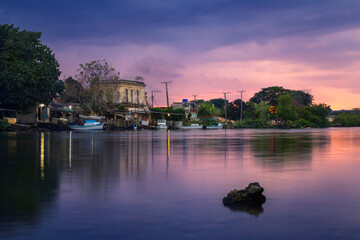 Fototapeta premium Calm pink sunset over a rural village on the river with moored boats