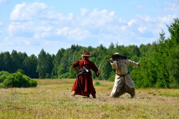 Close up on two medieval soldiers fighting by using old swords or scimitars spotted in the middle of a field and next to a vast forest or moor seen during a historical reenactment in Poland
