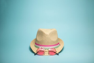 Straw hat adorned with a pink ribbon with a pair of sunglasses on a gray background