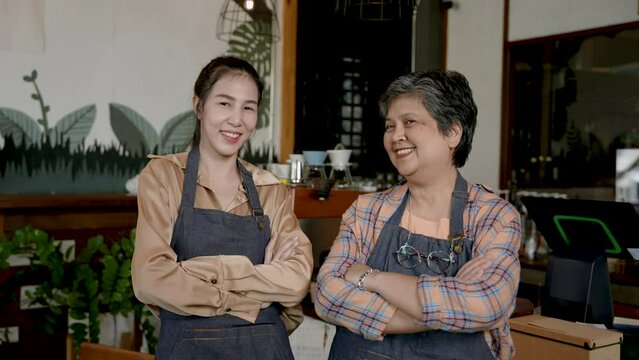 Elderly single mother Standing beside the beautiful daughter with arms folded, eyes met with happiness. Get ready to open coffee shop, small family business in morning of every day. woman owns cafe.