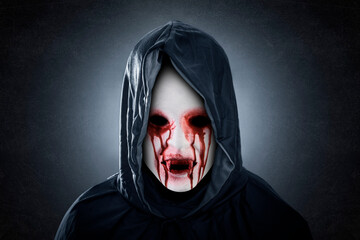 Creepy bloody vampire with hooded cape over dark misty background