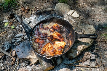 Pan of food being cooked over an open flame in an outdoor fire pit