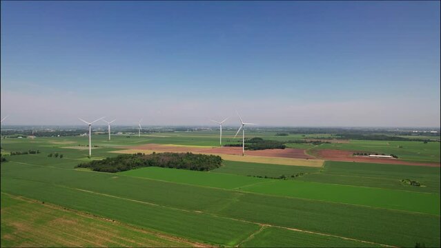 Drone shot over windmills in a green fields at countrysided under a blue sky