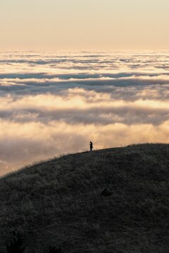 Silhouetted person standing on a hill, surveying a stunning landscape of rolling clouds