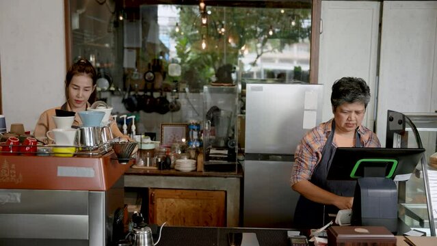 Small business coffee shop owner Asian elderly coffee shop owner Taking orders from customers who ordered online And tell the beautiful daughter barista to prepare coffee for customers.
