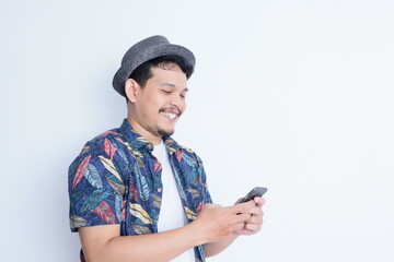 Young handsome asian man wearing casual beach shirt looking to his phone showing happy expression, isolated on white background.