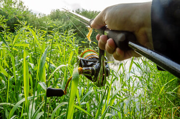 Male hand holding spinning rod on the background of the river.