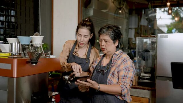Asian single mother Taking orders for a beautiful daughter who works as a barista making coffee for customers with a machine. In a small family business cafe. Working with passion.