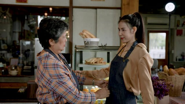 An elderly single mother helping her beautiful daughter tie an apron. To prepare to open a coffee shop, a small family business in the morning of every day. It's in an open cafe. shop owner woman