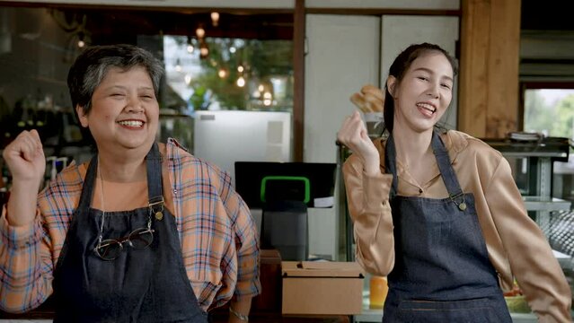 Elderly single mother dancing happily next to her daughter who owns a cafe Expressing joy to open a coffee shop, a small family business in the morning of every day. A woman owns a coffee shop.