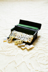 Selective focus view of vintage mother of pearl miniature dominoes spilling from their case set on pale lace background