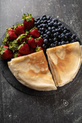 photo of a full plate of thin pancakes and fresh berries on a plate