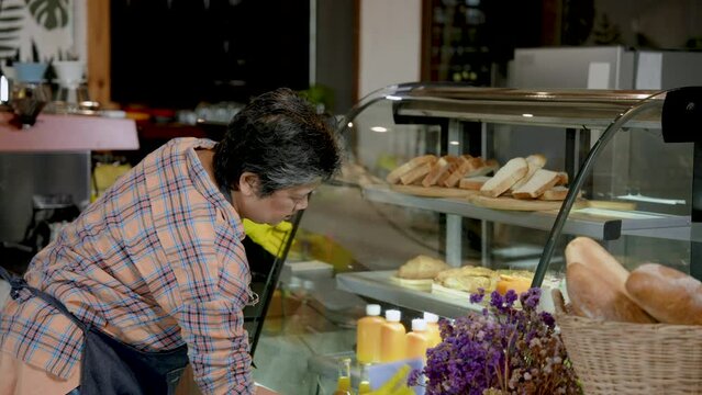 Coffee shop owner, elderly Asian woman, small family business. Cleaning shop and wiping glass of bakery cabinet. with refinement In evening after closing the shop to prepare to open the shop tomorrow.