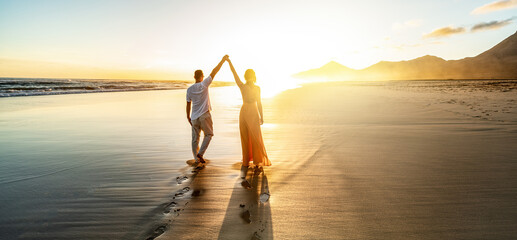 Fototapeta premium Romantic couple, man and woman holding hands enjoying sea sunset on beach during travel holidays vacation. Love, getaway, honeymoon, dating.