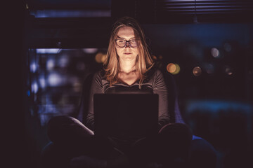Nighttime internet browsing. Woman's face illuminated by a laptop screen. - 630825675