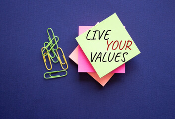Live your values symbol. Concept words Live your values on yellow steaky note with paper clips. Beautiful deep blue background. Business and Live your values concept. Copy space.