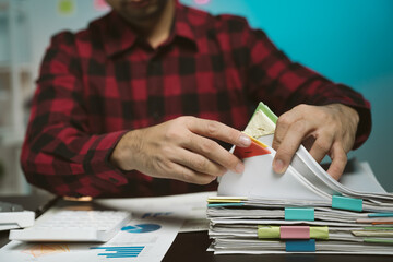 Businessman man working in stacks of papers searching for unfinished paperwork information on form check stack on table and checking financial papers in busy workload